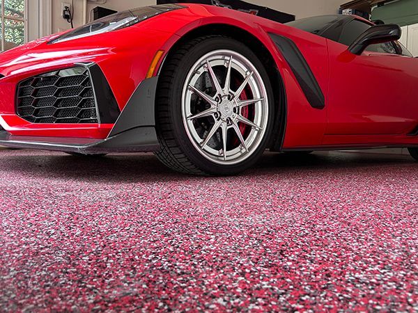 Red sports car parked on a speckled red and gray garage floor.