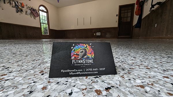 Business card on a colorful epoxy floor in a garage. Flynn Stone logo and contact info displayed.