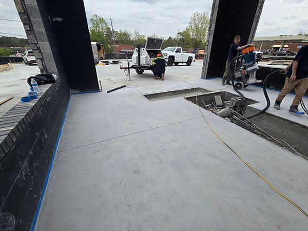 Workers preparing concrete surface, likely for a new driveway. Grey concrete, blue tape, outdoor setting.