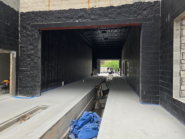 Tunnel-like structure with black brick walls, concrete floor, and open end. Construction site, daytime.