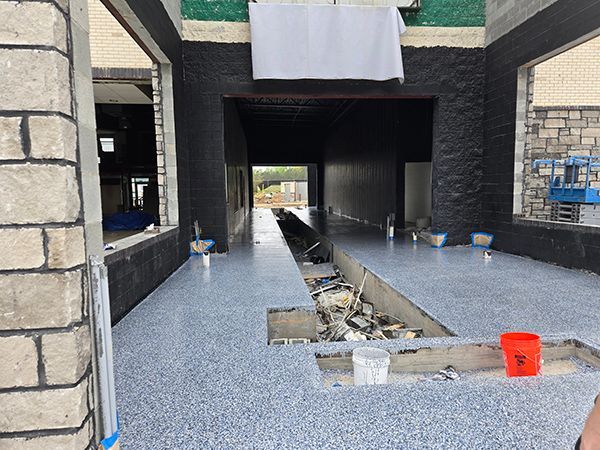 Interior of a building under construction with blue epoxy floor, brick walls, and large open windows.