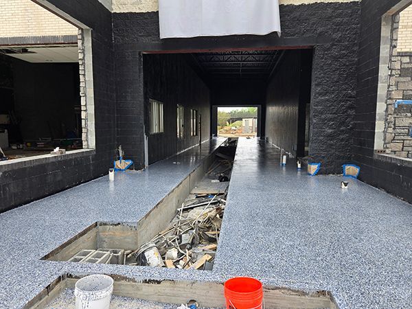 Interior of a building under construction with a long gray speckled floor, a pit, and black and gray walls.
