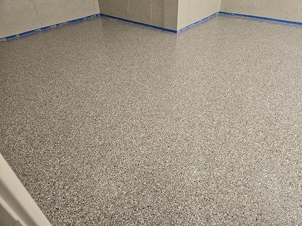 Gray speckled epoxy floor in a room, with blue tape along the walls.