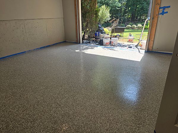 Epoxy-coated garage floor with speckled finish, sunlight streaming in doorway, with work supplies visible.