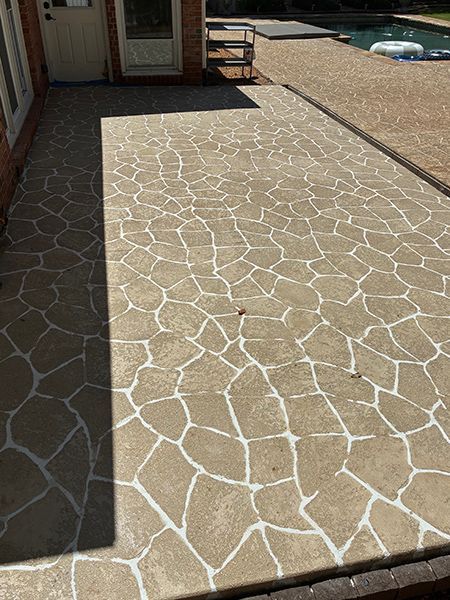 Stone-patterned concrete patio with white grout, next to a brick house and a pool.