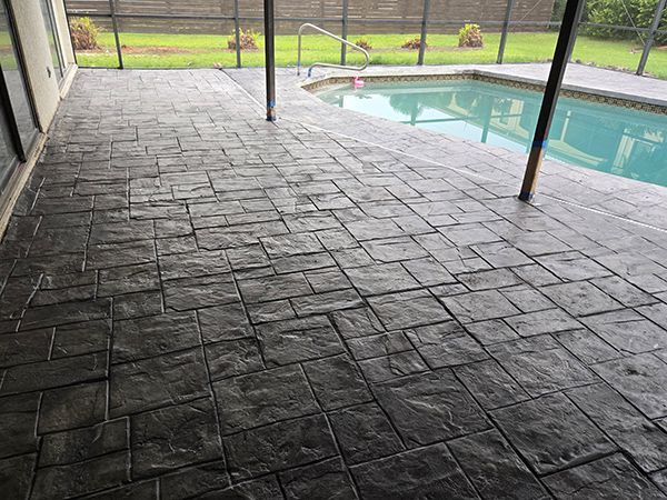 Stamped concrete patio by a pool. Dark gray, rectangular stone pattern.