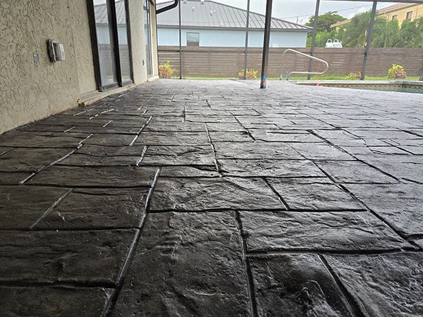 Dark gray stamped concrete patio, rectangular pattern, near a pool and house.