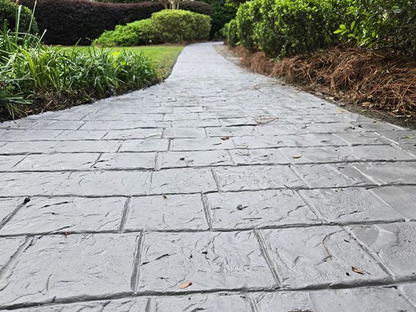 Stone-textured concrete pathway through a garden with green grass and bushes.