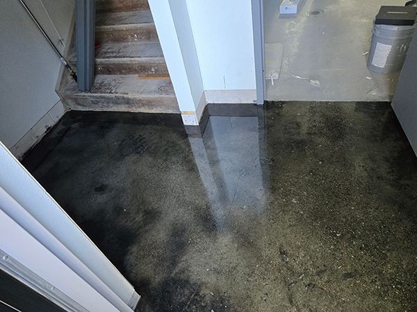 Dark, polished concrete floor. Staircase, white pillar, and door frame visible.