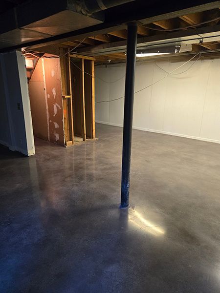 Empty basement with concrete floor, support beam, unfinished walls, and exposed ceiling joists.