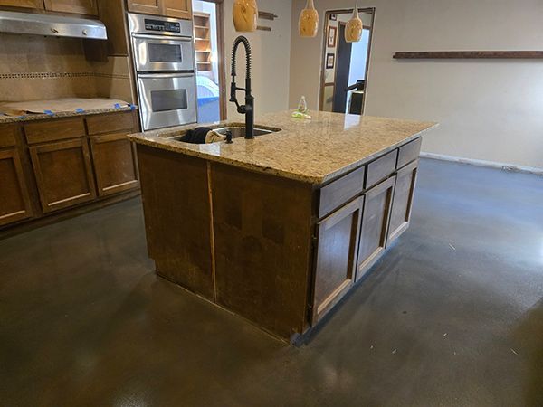 Kitchen island with granite countertop, dark cabinets, and black faucet. Concrete floor, brown cabinets, and stainless steel appliances.