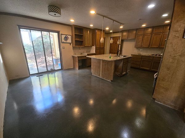 Kitchen with stained concrete floor, wood cabinets, and large island. Sliding glass door and recessed lighting.