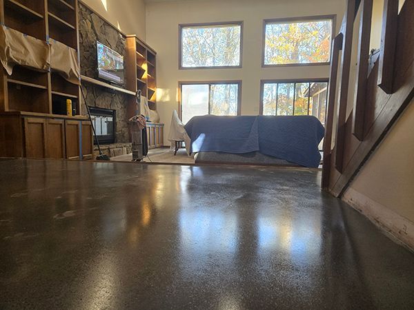 Living room with polished concrete floor, large windows, and a covered couch.