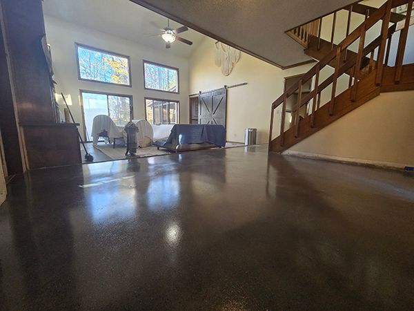 Polished dark gray concrete floor in a spacious living room with staircase and large windows.