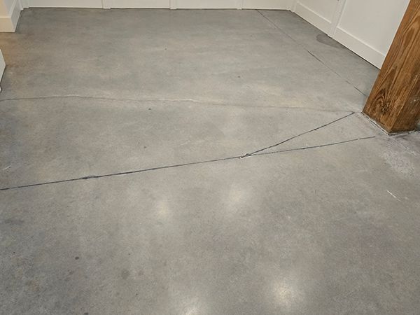 Gray concrete floor with long cracks, near a wooden support post.