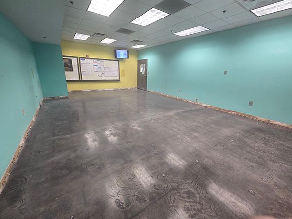 Empty room with teal and yellow walls, concrete floor, and fluorescent lights.