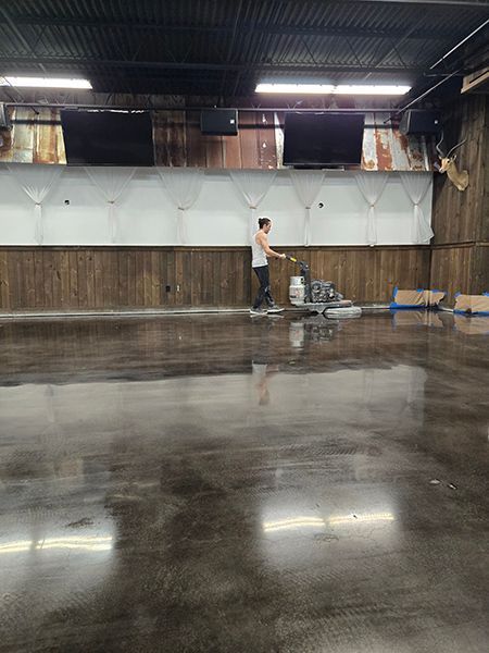 A man polishes a concrete floor in a large, empty room with wood paneling and a white wall.
