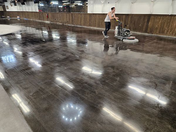 A person polishes a dark concrete floor with a machine in a large room.