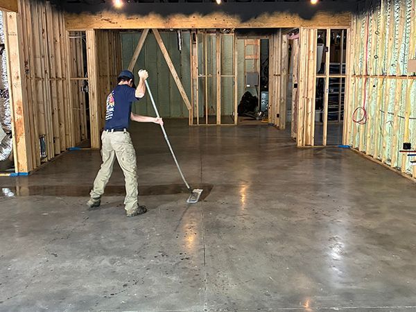 Man smoothing wet concrete floor in a room with exposed wooden framing.