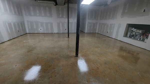 Empty unfinished basement with polished concrete floor, drywall walls, and support beams.