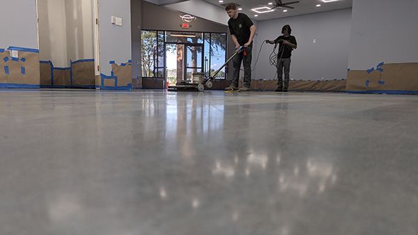 Two workers polishing a large, shiny concrete floor in a building interior.