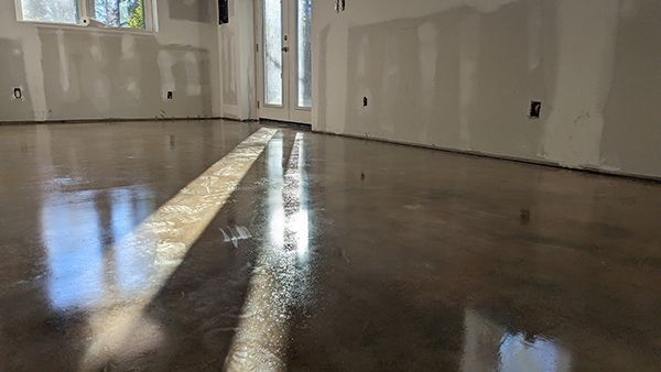 Shiny, polished concrete floor in a room with unfinished walls, sunlight streaming across the surface.