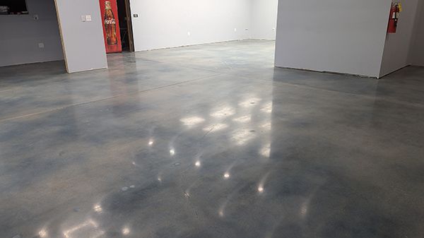 Polished concrete floor reflecting overhead lights in an empty room, with gray walls and a red door.