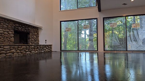Spacious room with stone fireplace, large windows, and glossy dark floor reflecting the outdoor view.