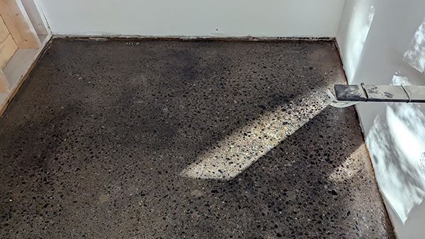 Dark gray concrete floor with a sunlit area and a drain.