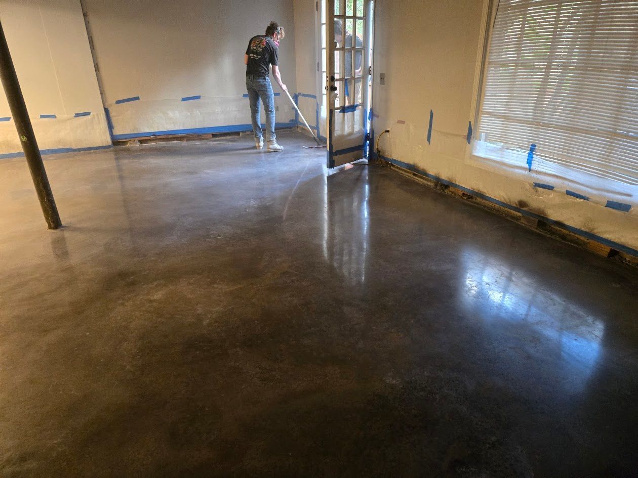 Person applying a coating to a polished concrete floor in a room.
