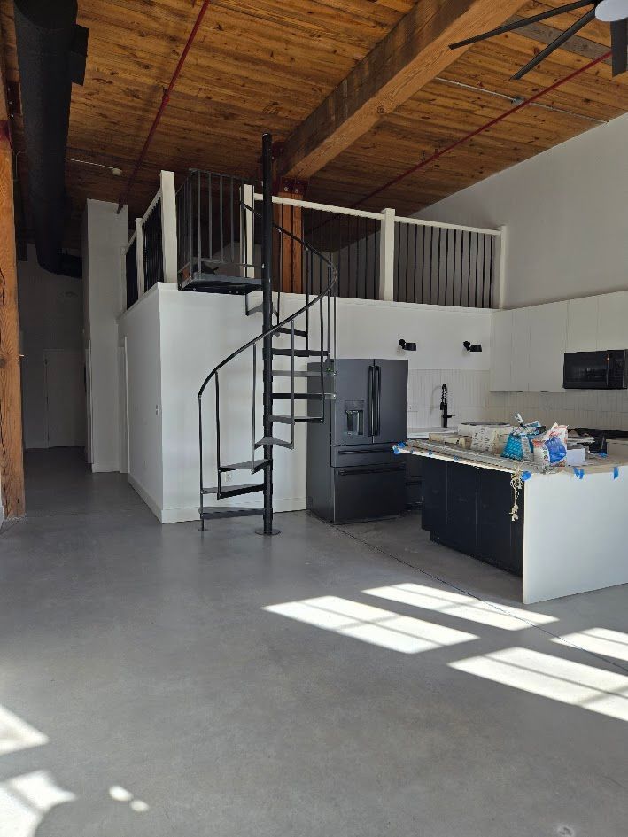 Loft with a spiral staircase, kitchen, and upper level with railing. Light streams in.