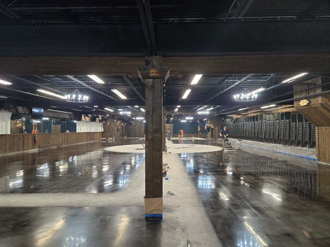 Large empty interior, concrete floor reflecting lights; wooden support beams and perimeter walls.