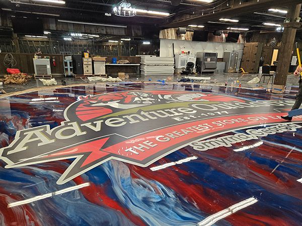 A large, colorful Adventure Quest logo on a painted floor inside a building; person walking by.