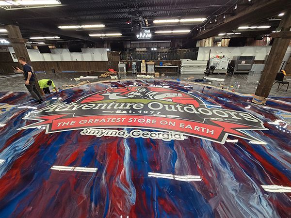 Workers installing Adventure Outdoors logo on a red, white, and blue epoxy floor in Smyrna, Georgia.