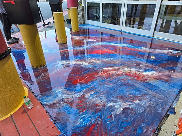 Epoxy-coated floor with swirling red, white, and blue colors at a building entrance, next to yellow support posts.