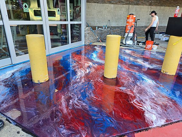 Epoxy floor with red, blue, and white swirls. Three yellow poles stand in the wet surface. Person stands nearby.