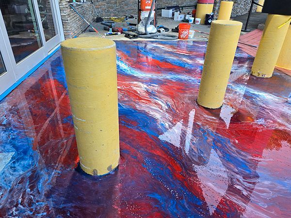 Epoxy-coated floor in red, blue, and white with yellow cylinder supports near a building.