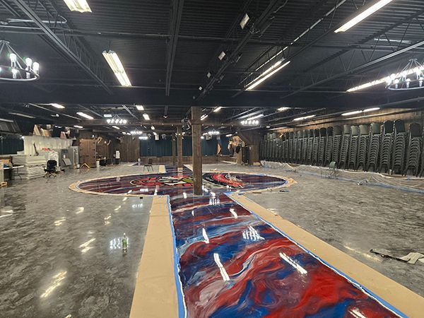Large, empty event space with epoxy flooring in progress; red and blue designs; black ceiling.