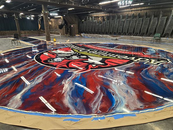 A circular epoxy floor with a school logo and red, white, and blue swirls. Large empty room with chairs in the background.