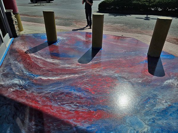 Metallic epoxy floor with red, white, and blue swirls, three wooden bollards casting shadows, person in the background.