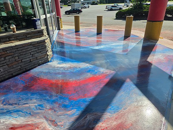 Outdoor flooring painted with red, white, and blue swirls. Sunlight casts shadows.