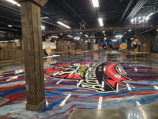 Indoor venue with a logo on the glossy floor, wooden beams, and tables; red, white, blue colors.