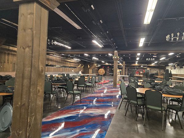 Large event space with tables and chairs, rustic wood columns, and a colorful floor.