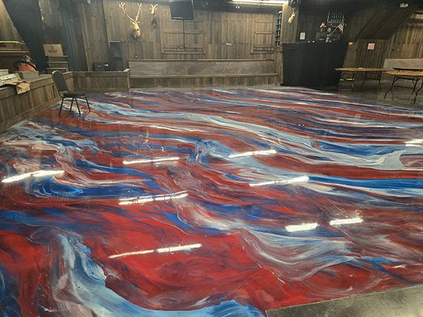 Red, white, and blue swirling epoxy floor in a wood-paneled venue. Stage area with chairs and speakers.