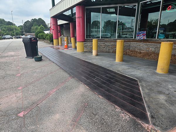 Exterior of a building with a dark walkway. Yellow bollards and pink parking lines are visible.