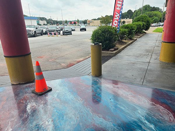 Entrance with colorful epoxy floor. Traffic cones, cars, and bushes in background.