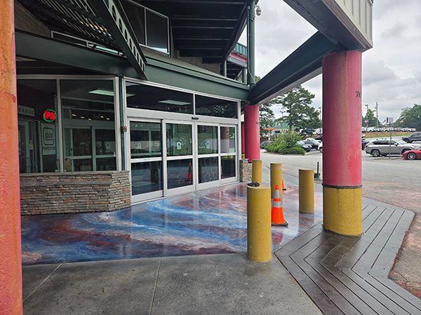 Entrance to a store with automatic sliding glass doors, red and yellow columns, and a decorative epoxy floor.