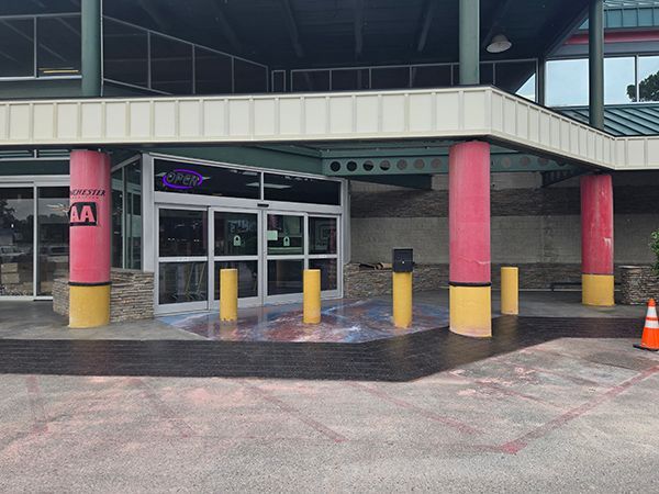 Entrance to a building with pink columns, a glass door, and yellow bollards.