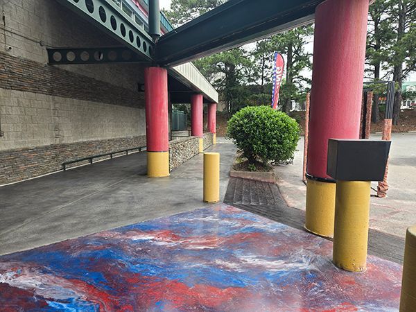 Exterior view: entrance with red/yellow pillars, colorful ground design, and a small bush.
