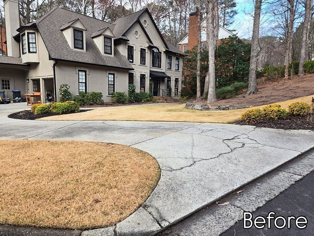 A cracked concrete driveway in front of a two-story house with brown grass.